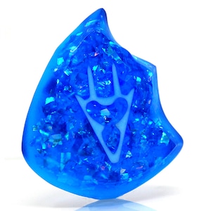 May include: A blue resin guitar pick with a white, stylized, three-pronged design.