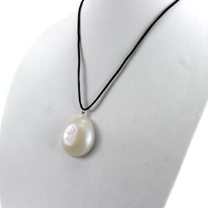 May include: A white pearl pendant necklace with a black cord. The pearl is oval shaped and has a small flower design carved into it.