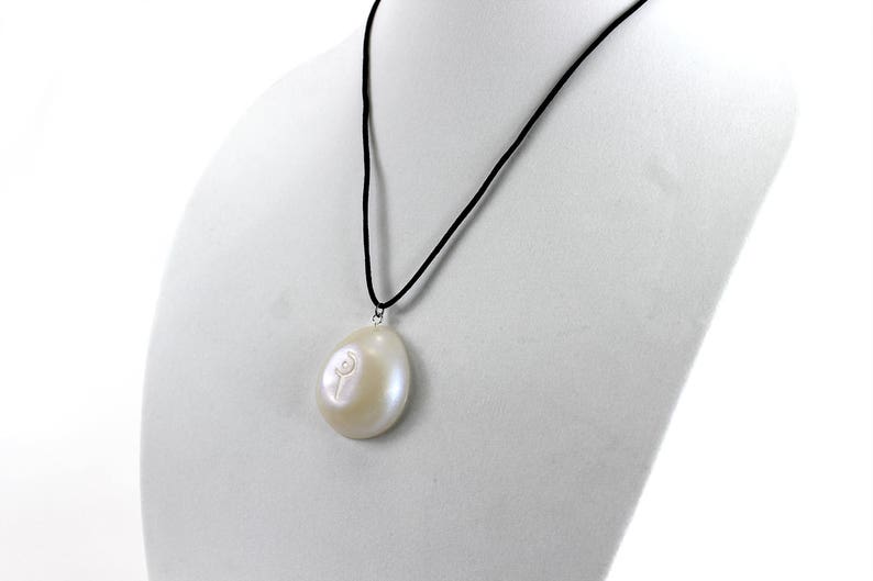 May include: A white pearl pendant necklace with a black cord. The pearl is oval shaped and has a small flower design carved into it.