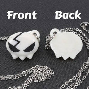 May include: A silver chain necklace with a white pendant featuring a black lightning bolt and eyes. The back of the pendant is blank.