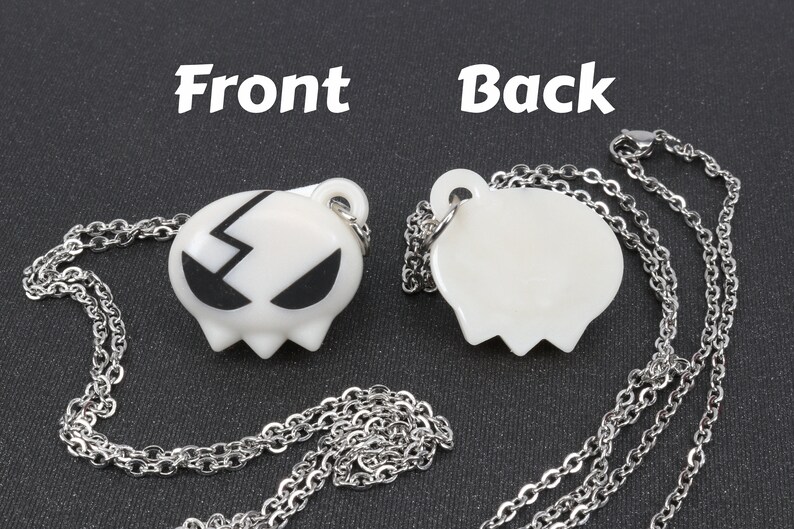 May include: A silver chain necklace with a white pendant featuring a black lightning bolt and eyes. The back of the pendant is blank.