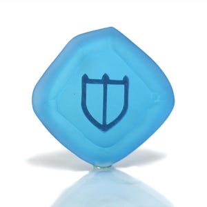 Puede incluir: Un dado de vidrio esmerilado azul claro con un s&iacute;mbolo de escudo grabado en la cara.