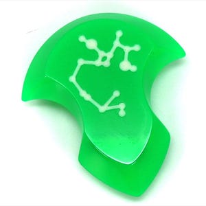 Op de afbeelding: Een groene, doorschijnende, halvemaanvormige hanger met een witte omtrek van het sterrenbeeld Boogschutter.