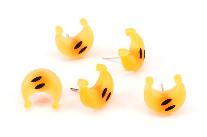以下が含まれることがあります： 黒い目をつけた黄色の三日月型のイヤリングが5つセットになっています。イヤリングはプラスチック製で、銀色のポストが付いています。