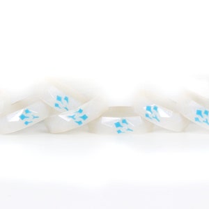 May include: A set of eight white skateboard wheel risers with a blue geometric design. The risers are stacked on top of each other.