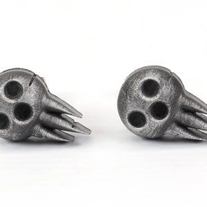 Peut inclure: Une paire de boucles d'oreilles en argent en forme de cr&acirc;ne avec trois trous dans le cr&acirc;ne et un design &agrave; pointes.