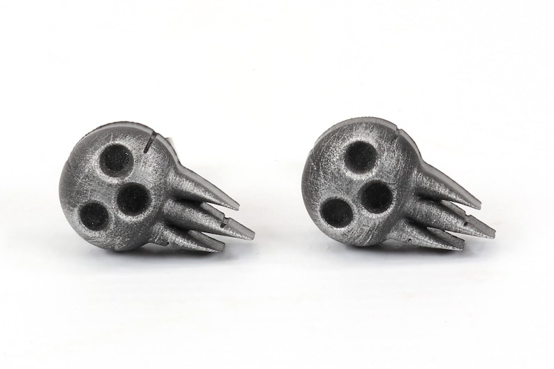 Peut inclure: Une paire de boucles d'oreilles en argent en forme de cr&acirc;ne avec trois trous dans le cr&acirc;ne et un design &agrave; pointes.