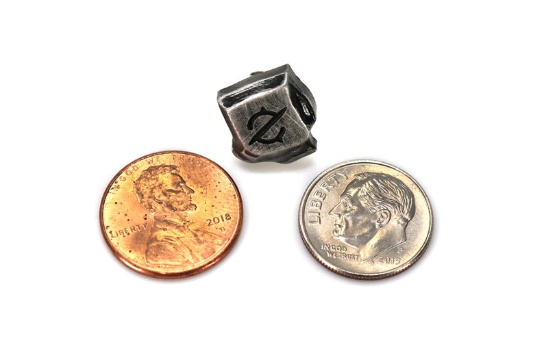 May include: A silver metal dice with a stylized "Z" symbol on each face. The dice is about the size of a US penny.