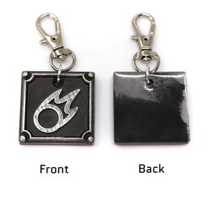 May include: A silver metal keychain with a black square charm featuring a silver flame symbol on the front and a blank surface on the back.