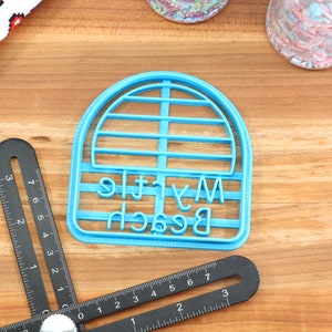 May include: A blue plastic cookie cutter shaped like a beach umbrella with the words "My Little Beach" written on it.
