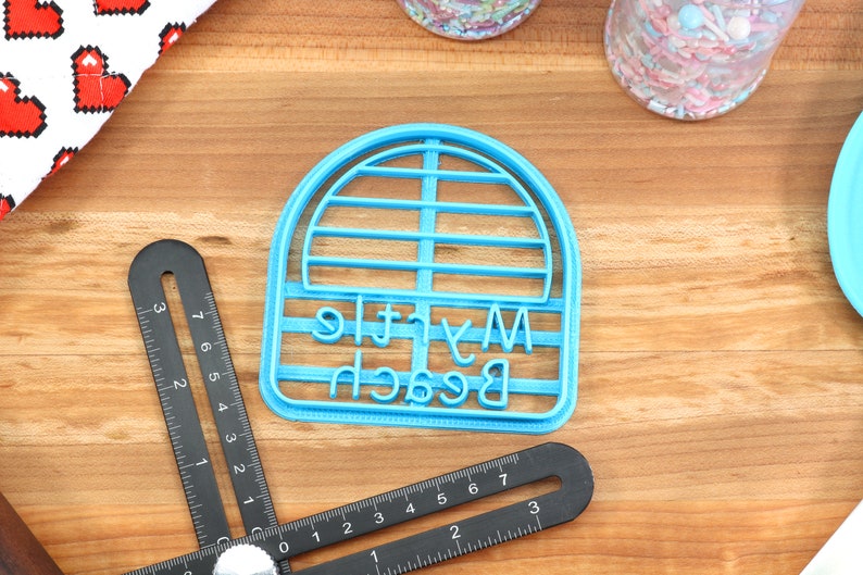 May include: A blue plastic cookie cutter shaped like a beach umbrella with the words "My Little Beach" written on it.