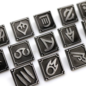 May include: A set of 16 silver metal pins with different symbols, each pin is square shaped with rounded corners and a black background.