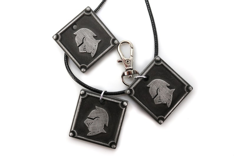 May include: Three silver-toned pendants with a knight's helmet design. The pendants are attached to black cords and one has a silver-toned lobster clasp.