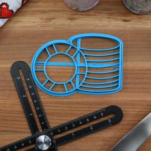 May include: Two blue plastic cookie cutters, one shaped like a circle with a smaller circle inside and the other shaped like a stack of coins. The cutters are on a wooden surface.