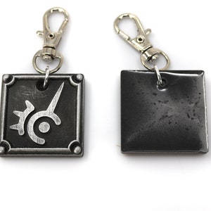 May include: Two silver keychains with a square metal charm. One charm features a silver design of a stylized sword and circle. The other charm is plain.
