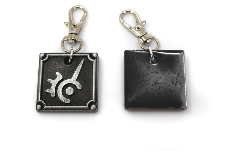 May include: Two silver keychains with a square metal charm. One charm features a silver design of a stylized sword and circle. The other charm is plain.