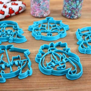 May include: Set of six blue plastic cookie cutters shaped like cartoon characters. The cutters are on a wooden surface.