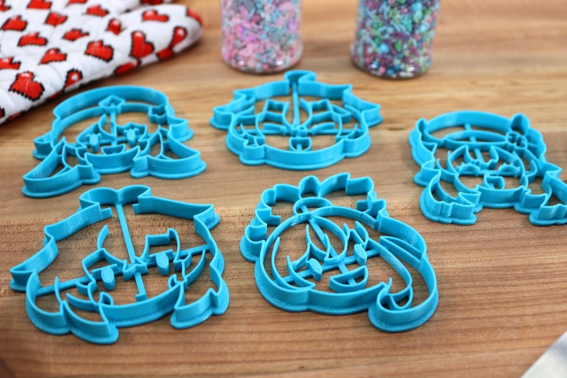May include: Set of six blue plastic cookie cutters shaped like cartoon characters. The cutters are on a wooden surface.