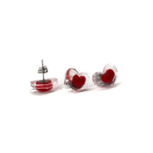 Puede incluir: Un par de pendientes transparentes en forma de coraz&oacute;n con corazones rojos en su interior. Los pendientes tienen postes de plata.