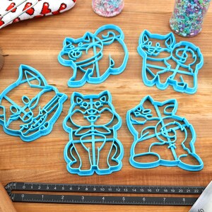 May include: Set of six blue plastic cookie cutters shaped like dogs. The cutters are on a wooden surface with a ruler and a rolling pin.