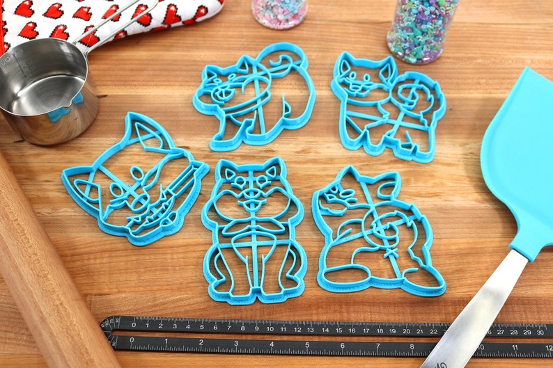 May include: Set of six blue plastic cookie cutters shaped like dogs. The cutters are on a wooden surface with a ruler and a rolling pin.