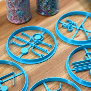 May include: Six blue plastic cookie cutters with different geometric designs. The cutters are on a wooden surface.
