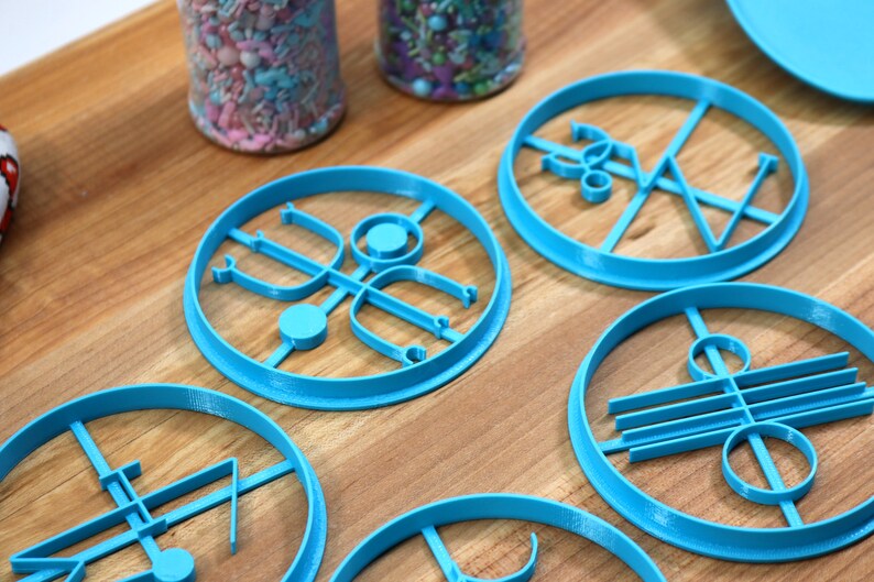 May include: Six blue plastic cookie cutters with different geometric designs. The cutters are on a wooden surface.
