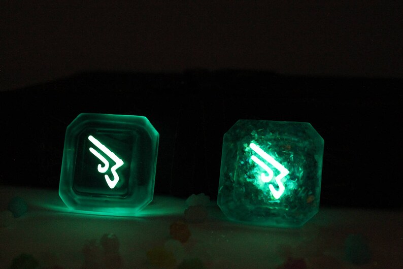 May include: Two glowing green resin dice with a white symbol on each face. The symbol is a stylized wing with a number 3 in the center.