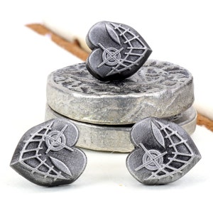 May include: Three silver heart-shaped metal stamps with a geometric design. The stamps are on a white surface.