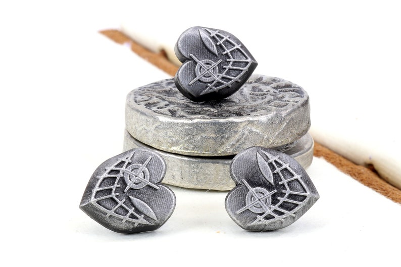 May include: Three silver heart-shaped metal stamps with a geometric design. The stamps are on a white surface.