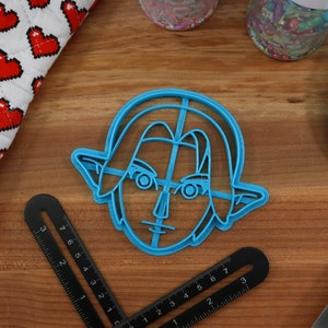 May include: Blue plastic cookie cutter shaped like Link from the Legend of Zelda video game series. The cutter is on a wooden surface.