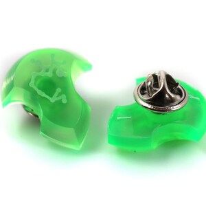 May include: Two green plastic pinback buttons with a white design. One button has a pinback attached. The design is a constellation of stars.