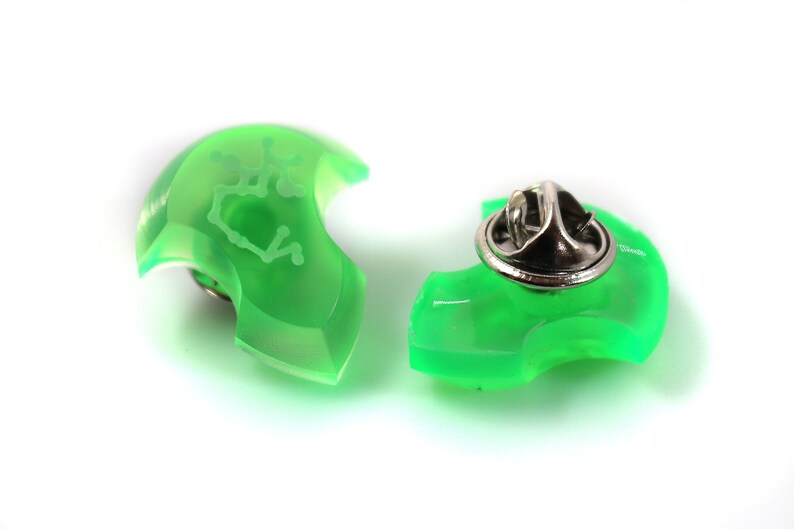 May include: Two green plastic pinback buttons with a white design. One button has a pinback attached. The design is a constellation of stars.
