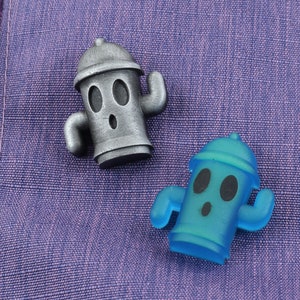 May include: Two fire hydrant figurines, one silver and one blue, with cartoon faces and arms. The figurines are on a purple fabric background.