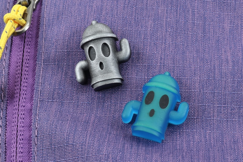 May include: Two fire hydrant figurines, one silver and one blue, with cartoon faces and arms. The figurines are on a purple fabric background.