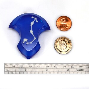 May include: A blue resin dice with a white constellation design. The dice is about the size of a US penny.