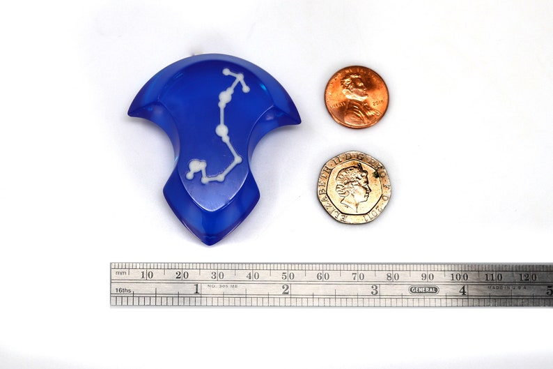 May include: A blue resin dice with a white constellation design. The dice is about the size of a US penny.