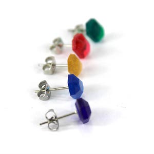 May include: Five pairs of stud earrings with different colored gemstones. The earrings are silver and have a post back. The gemstones are green, red, yellow, blue, and purple.