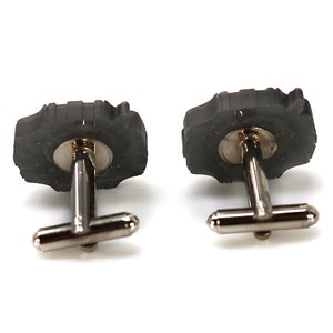 May include: A pair of cufflinks with a black, textured, circular design. The cufflinks have a silver metal backing.