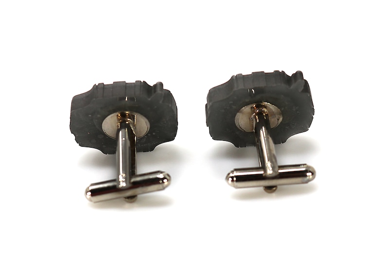 May include: A pair of cufflinks with a black, textured, circular design. The cufflinks have a silver metal backing.