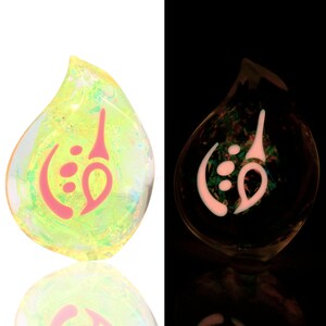 May include: A teardrop-shaped glass pendant with a pink and white design. The pendant glows in the dark.