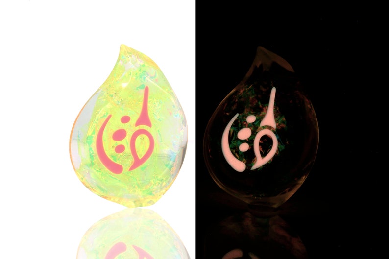 May include: A teardrop-shaped glass pendant with a pink and white design. The pendant glows in the dark.
