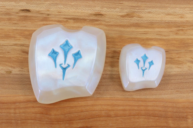 Pu&ograve; includere: Due oggetti decorativi in ceramica bianca iridescente con un design a stella blu a tre punte stilizzato.