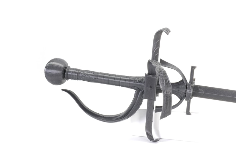 May include: A grey metal sword with a decorative handle and a curved guard. The sword has a black blade and a round pommel.