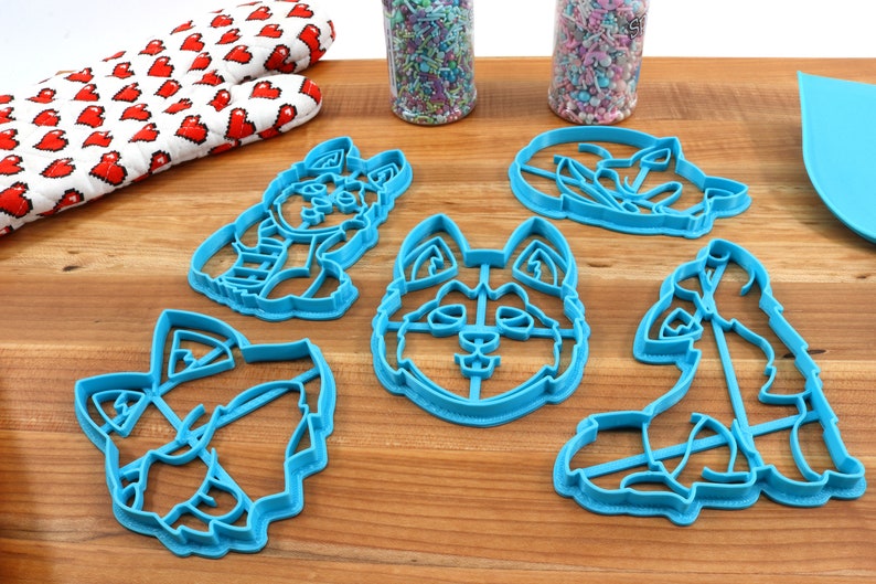 K&ouml;nnte beinhalten: Satz mit f&uuml;nf blauen Plastik-Ausstechern in Form verschiedener Hunderassen. Die Ausstecher liegen auf einer Holzoberfl&auml;che.