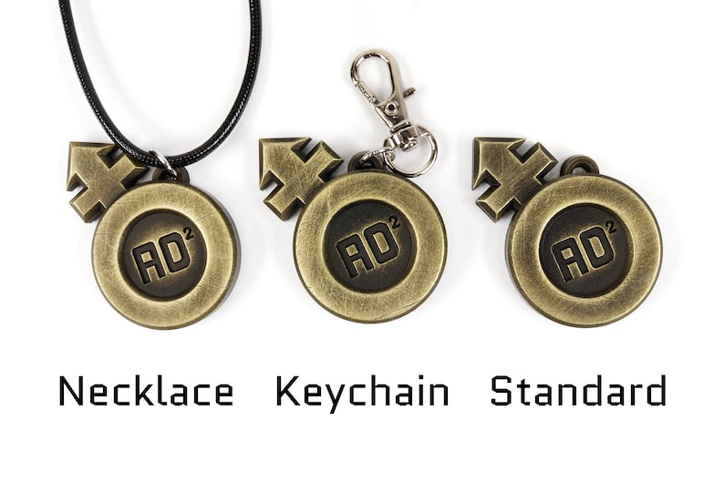 May include: Three versions of a gold-colored metal pendant with a black symbol and the text "AD2". The pendant is shown as a necklace, a keychain, and a standard pendant.