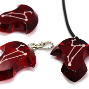 May include: Three red glass pendants with a white constellation design. The pendants are shaped like a teardrop with a pointed tip. One pendant is on a black cord necklace, one is on a silver chain, and one is loose.