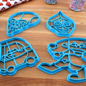 Puede incluir: Cuatro cortadores de galletas de pl&aacute;stico azul con forma de personajes de la pel&iacute;cula animada "Onward". Los cortadores est&aacute;n sobre una superficie de madera.