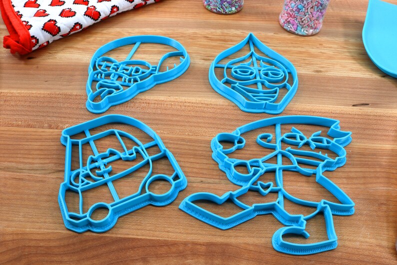 Puede incluir: Cuatro cortadores de galletas de pl&aacute;stico azul con forma de personajes de la pel&iacute;cula animada "Onward". Los cortadores est&aacute;n sobre una superficie de madera.