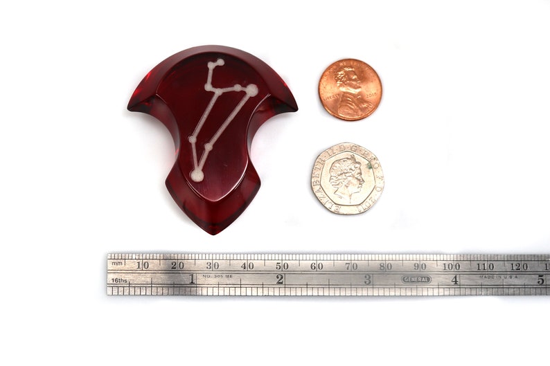 May include: A red, resin, dice with a white constellation design. The dice is about the size of a US penny.
